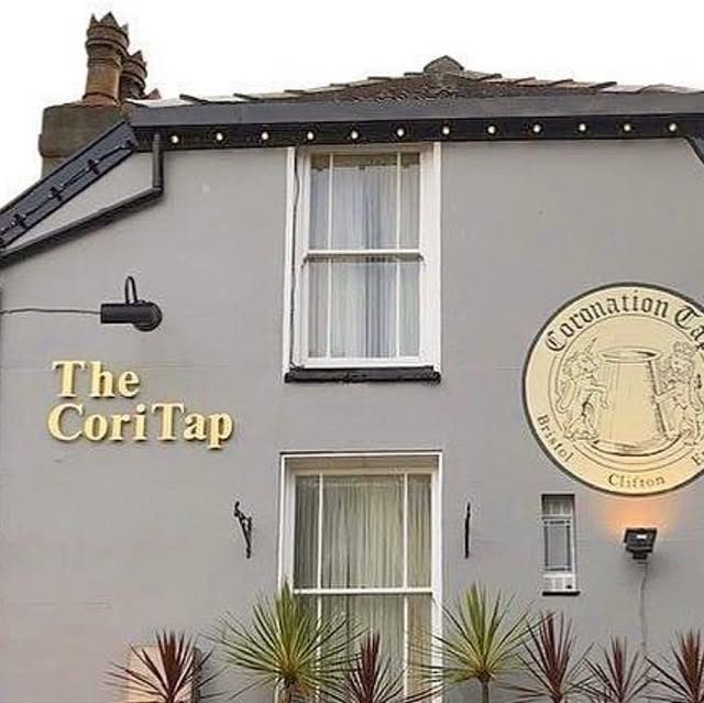 The white-painted front of the pub with 'The CoriTap' lettering and the round Coronation Tap plaque