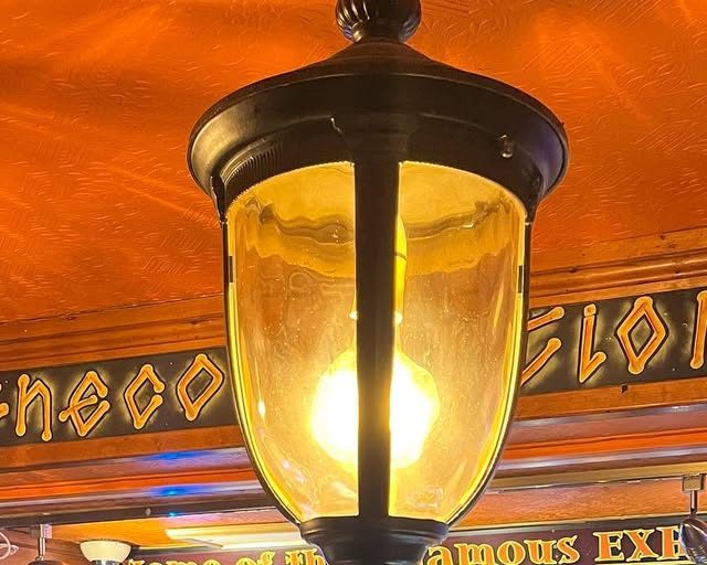 A brass lantern glowing under the orange bar ceiling, with the gold lettering 'Home of the infamous Exhibition' behind it