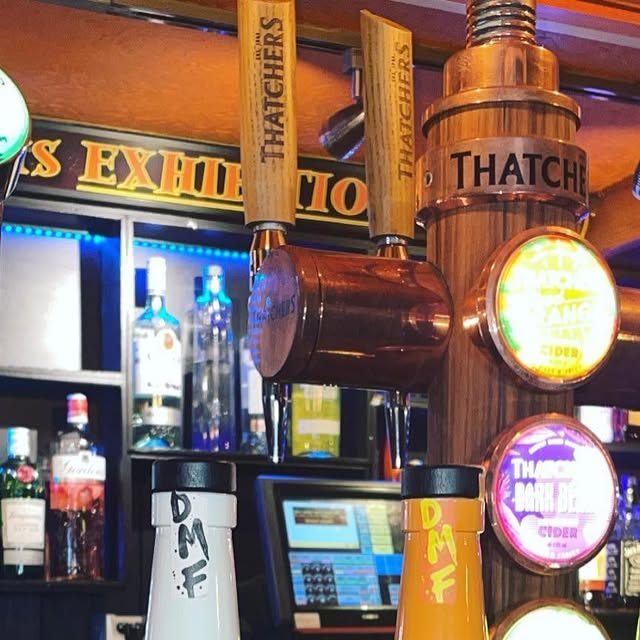 Thatchers cider pumps on the bar in front of the lit Exhibition gantry